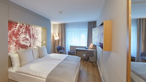 Habitación de hotel con cama, escritorio, silla y un espejo grande.