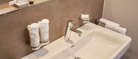 A modern bathroom with a large white sink, chrome faucet, and two towel dispensers.