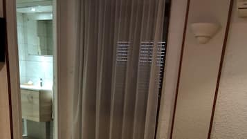 A hotel room with a bed, a bathroom visible through a glass door, and a cityscape view through the window.