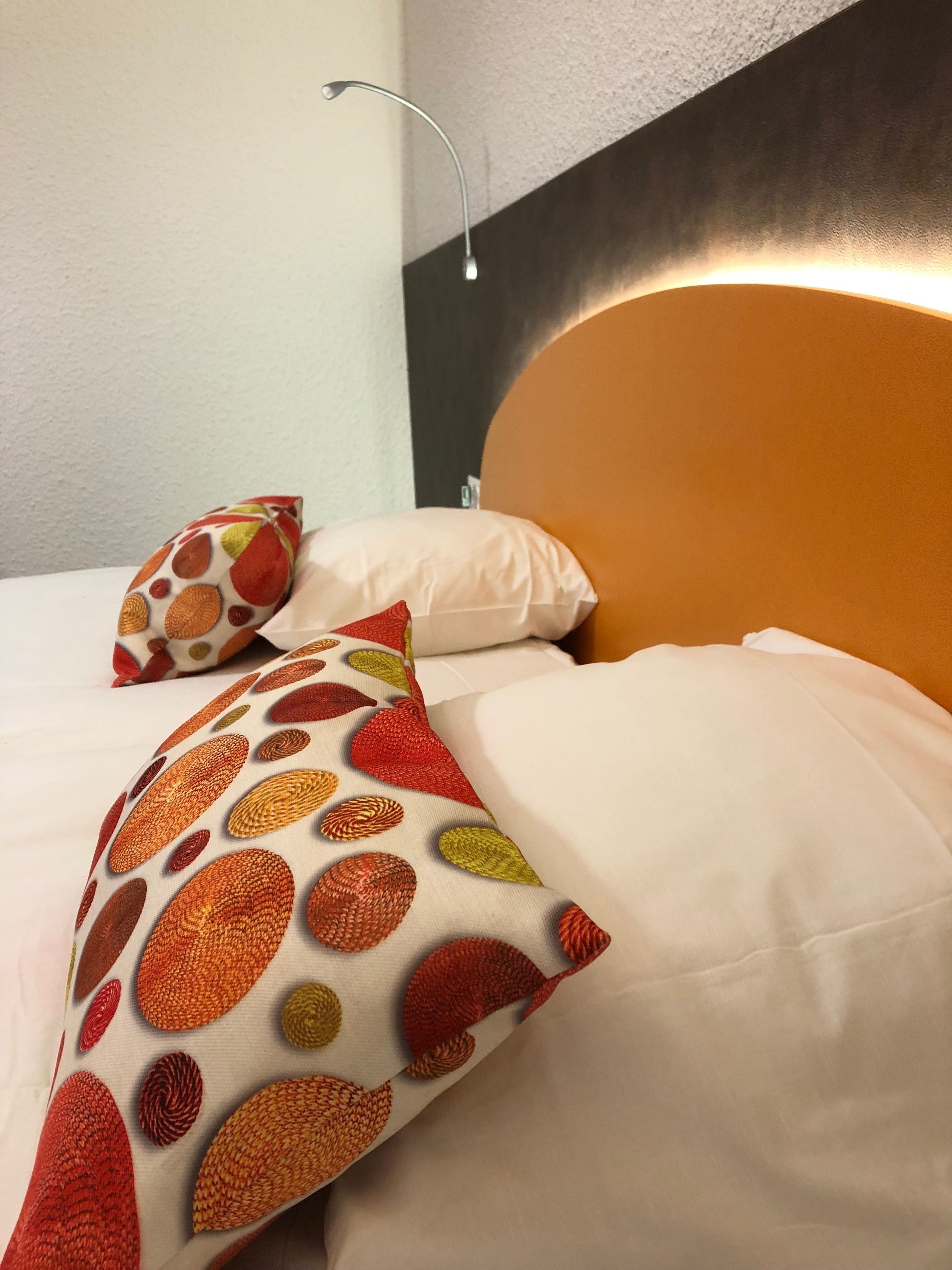 A hotel room with a bed, white bedding, and a headboard with a light fixture.