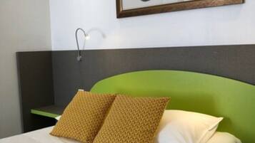 A hotel room with a green upholstered headboard, a bed with white and yellow bedding, and a framed picture of a yellow car on the wall.