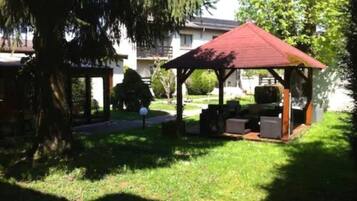 A covered outdoor seating area with a red roof, surrounded by grass and trees.