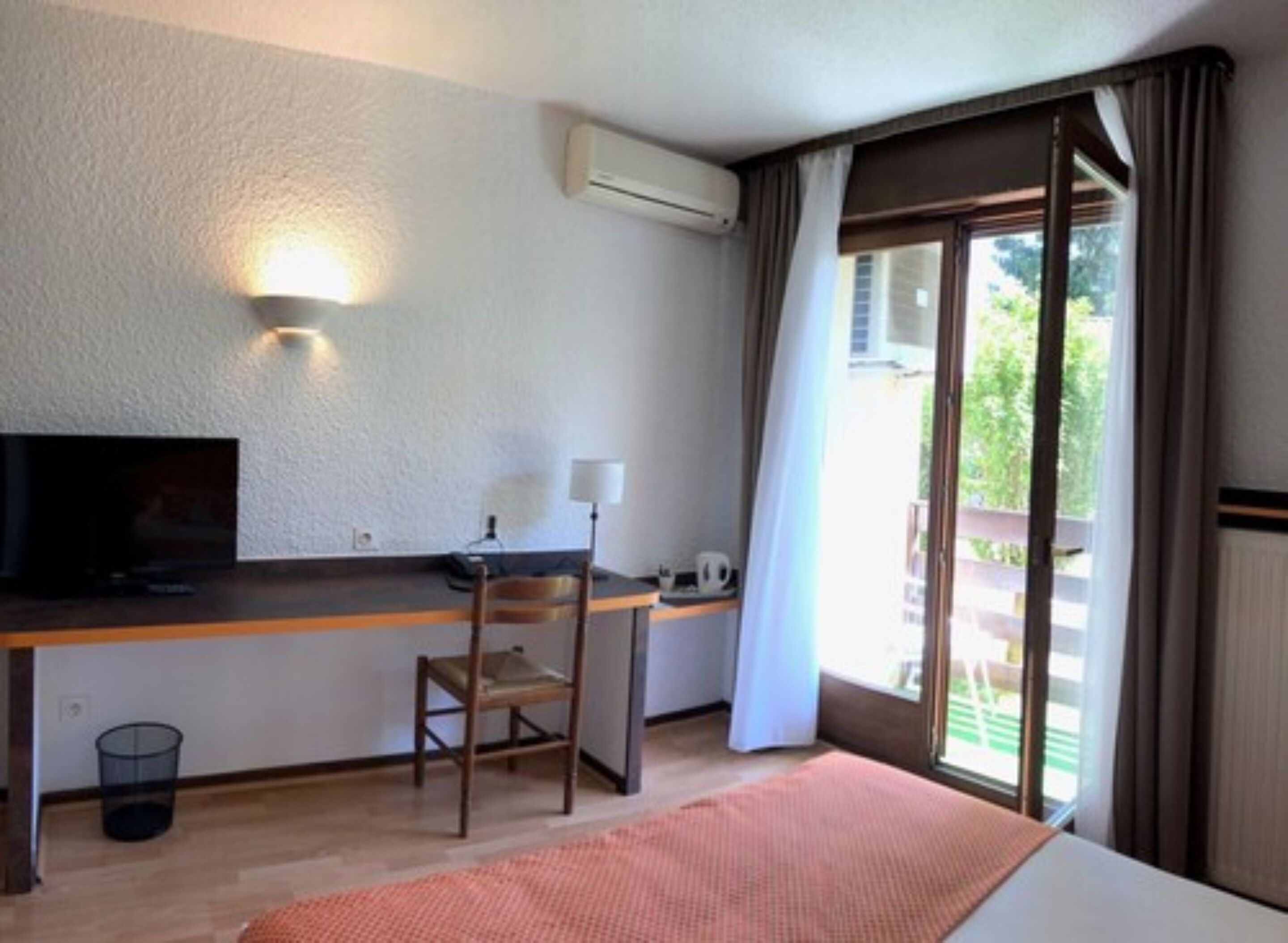 Une chambre d’hôtel avec un lit, un bureau et une chaise, une télévision et une fenêtre avec des rideaux.