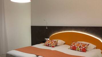 A double bed with a headboard, two pillows, a red pendant light, and a bedside table with a lamp.