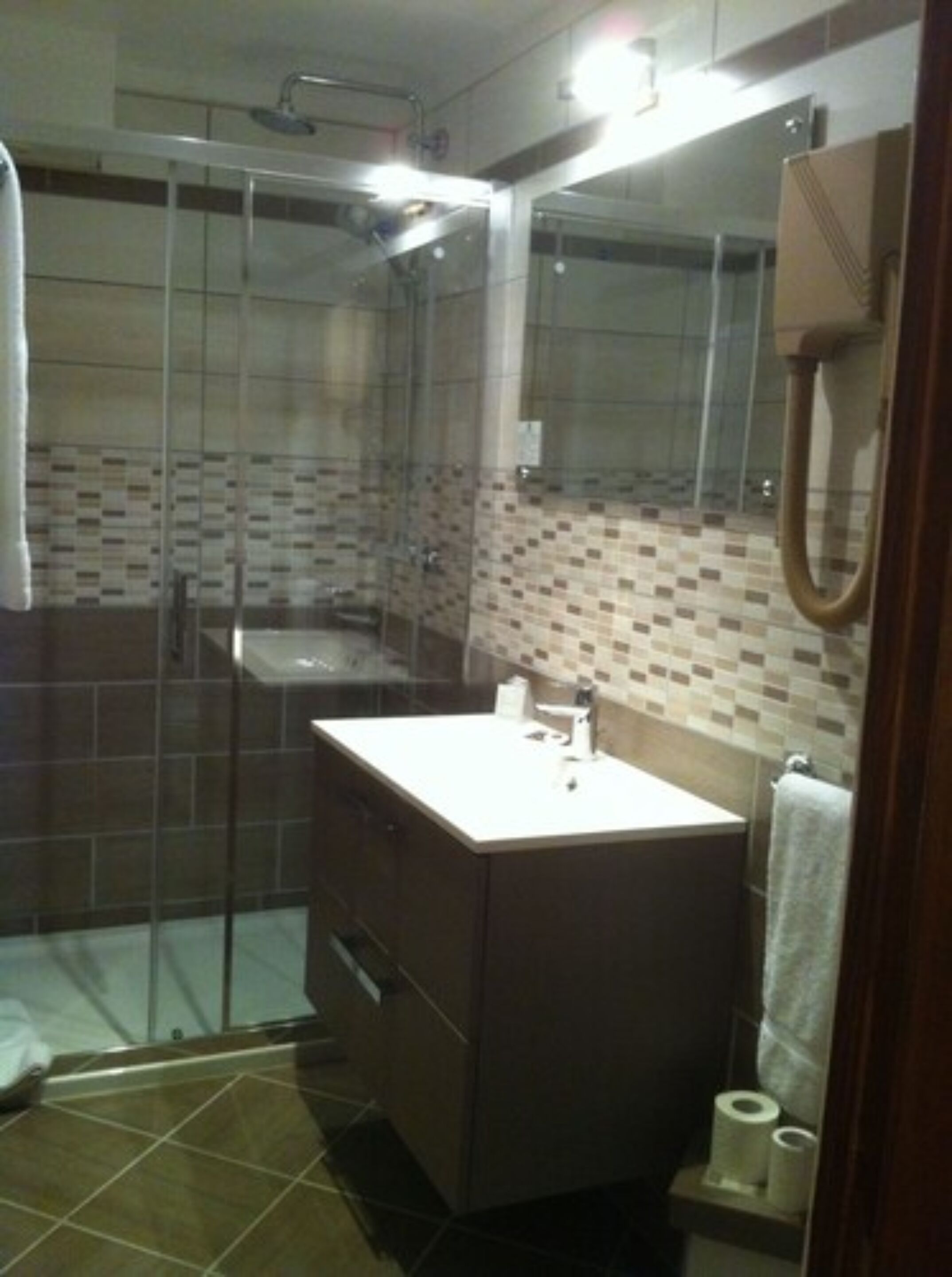 A bathroom with a glass shower enclosure, a sink with a mirror, and a tiled backsplash.