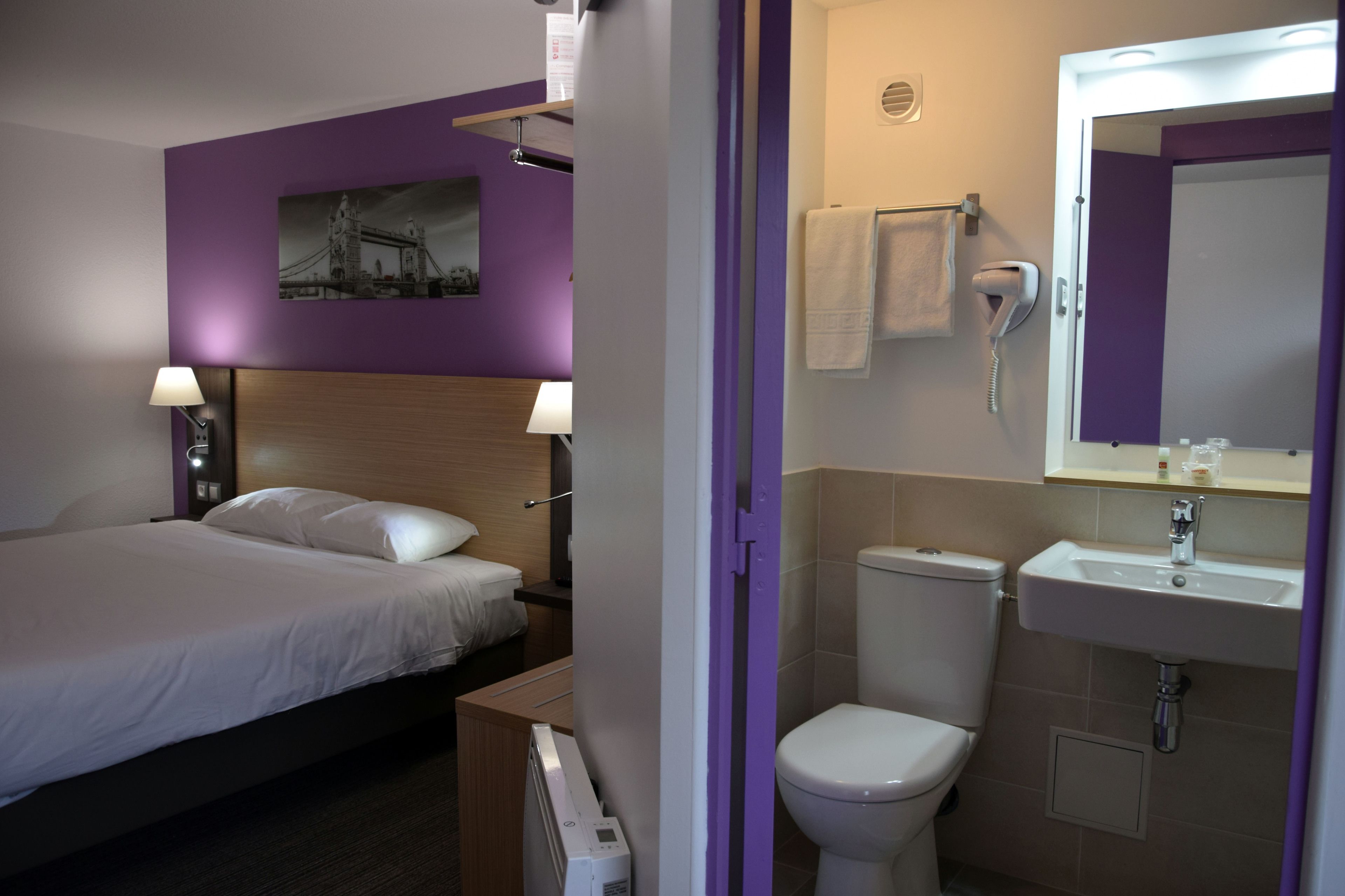 A hotel room with a bed, bedside lamps, a bathroom with a toilet, sink, and towel rack.