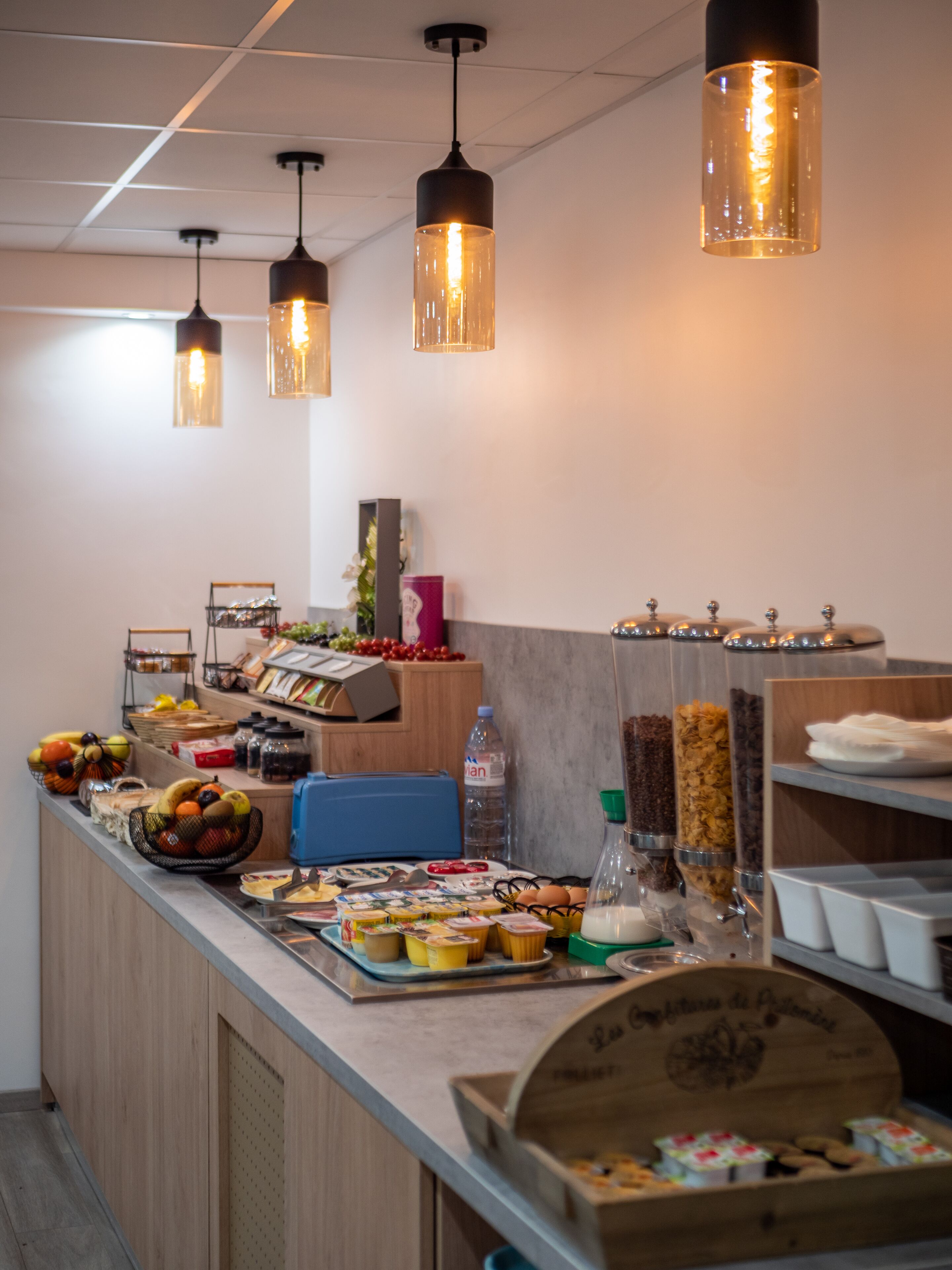 A breakfast bar with various food items, a water dispenser, and hanging pendant lights.
