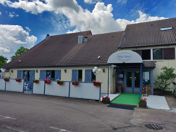 A hotel with a tiled roof, a covered entrance, and flower boxes along the side. - Hotel Restaurant Bleu France (Eragny)