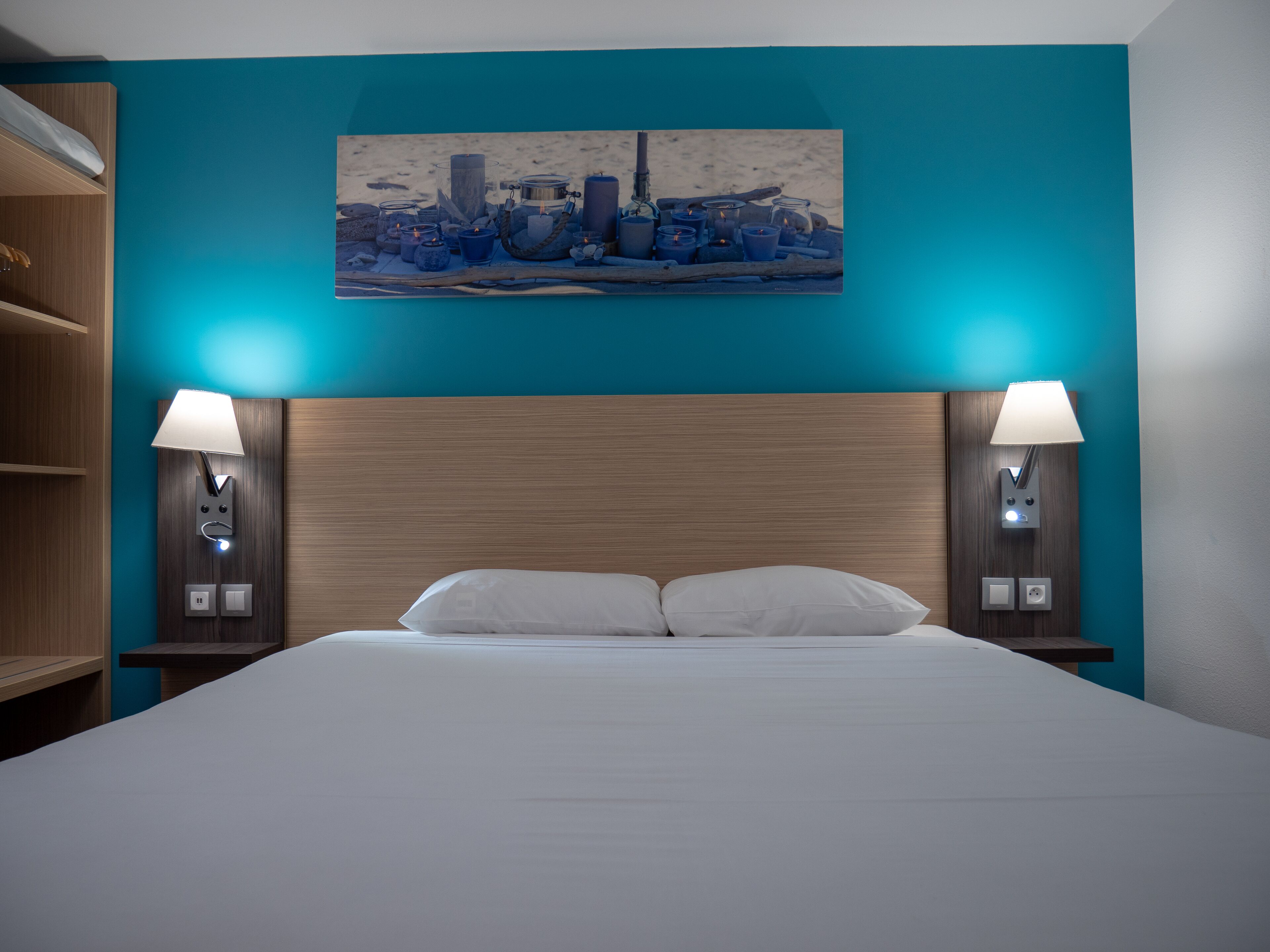 Ein Hotelzimmer mit einem großen Bett, zwei Nachttischen mit Lampen, einem Stadtbild an der Wand und teal-farbenen Wänden.