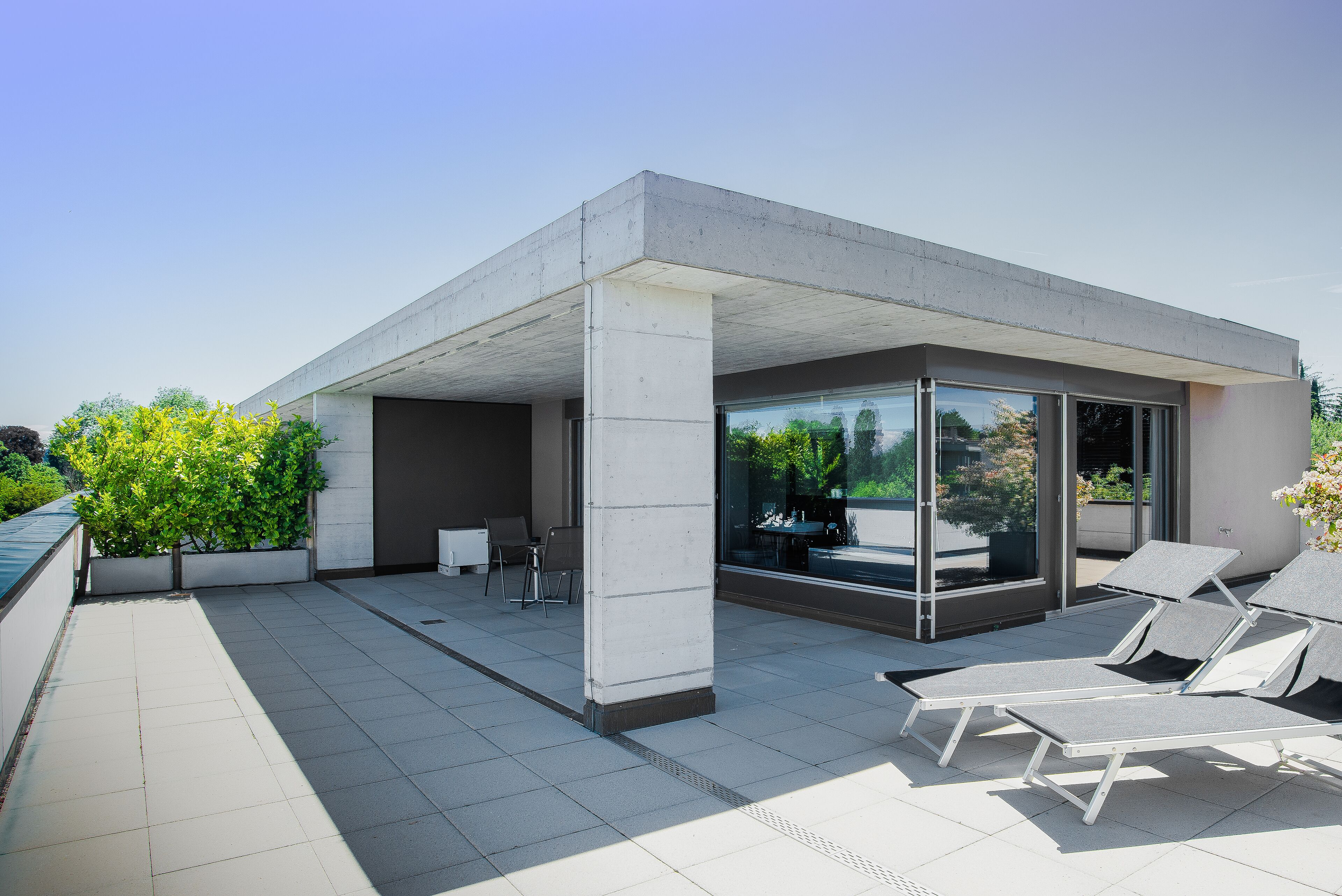 Eine moderne Außenpatio mit Betonböden, Glaswänden und Lounge-Stühlen.