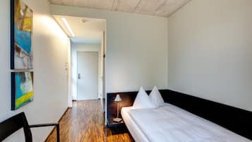 Een hotelkamer met een houten vloer, een bed met witte lakens, een bureau met een stoel en een schilderij aan de muur.