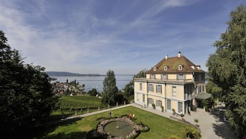 Un edificio grande e histórico con un jardín formal y una fuente circular, con vistas a un cuerpo de agua.
