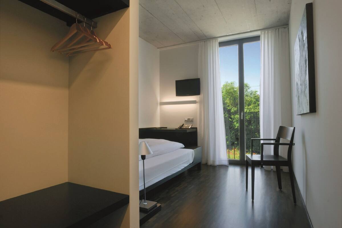 Ein modernes Hotelzimmer mit Bett, Schreibtisch, Stuhl, Fernseher und einem Balkon mit Blick.