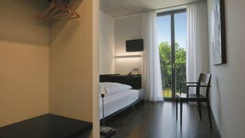 A modern hotel room with a bed, a desk, a chair, a TV, and a balcony with a view.