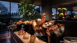 A kitchen counter with various breads and pastries, a cutting board, and a bowl of apples. - Hotel Kreuzlingen am Hafen (Kreuzlingen)