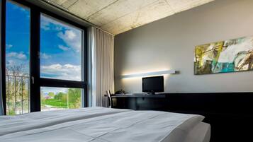 Una habitación de hotel con una cama grande, un escritorio con computadora, televisor y un cuadro en la pared.