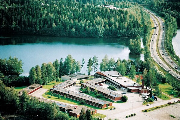 An aerial view of a campus with multiple buildings, a parking lot, and a road curving around a lake.
