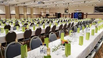 A conference room with rows of tables set for a meeting, equipped with chairs, tables, and green tablecloths.