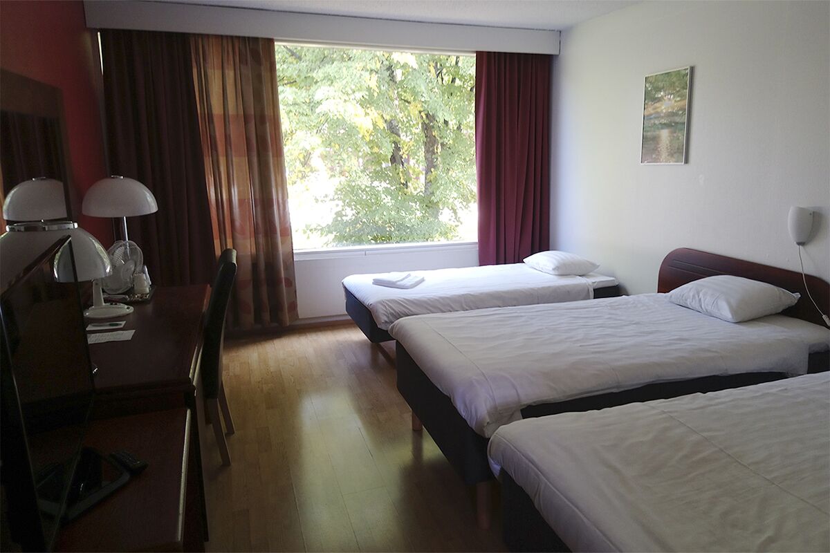Una habitación de hotel con dos camas individuales, un escritorio con lámpara y un ventanal con cortinas.