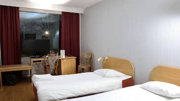 Habitación de hotel con dos camas individuales, un escritorio con silla, un armario y un ventanal con cortinas.