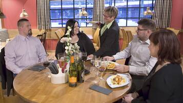 Un grupo de personas cenando en una mesa redonda, con botellas y copas de vino.