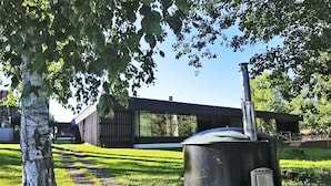 Una casa moderna con un contenedor metálico grande en el patio, un árbol y un cielo despejado.