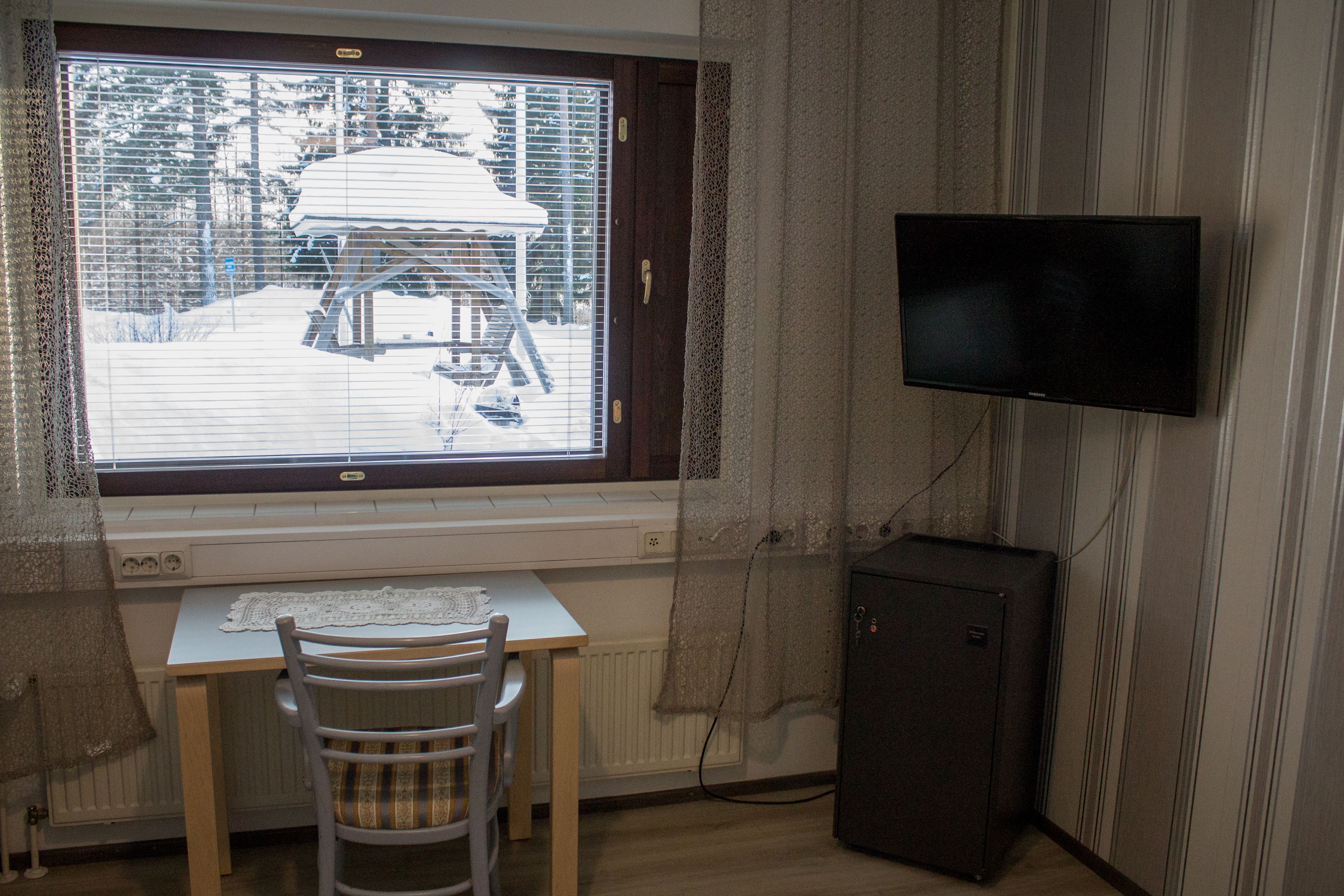 Huoneessa on ikkuna, josta avautuu näkymä lumiseen maisemaan, seinälle asennettu televisio, pieni pöytä ja tuoli sekä patteri ikkunan alla.