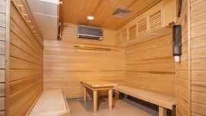 A sauna room with wooden walls, a bench, a table, and a wall-mounted heater. - Hotelli Vuolake (Laukaa)