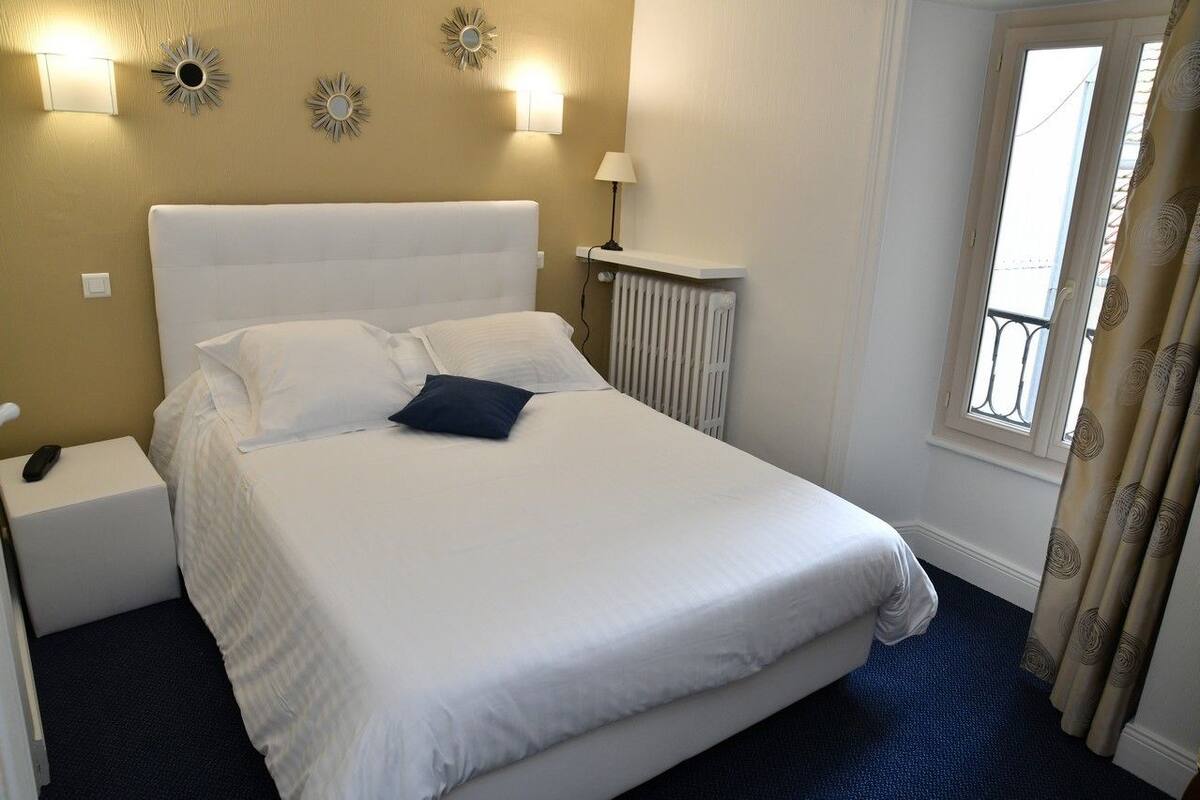 A hotel room with a large bed, a bedside table, a lamp, and a window with curtains.