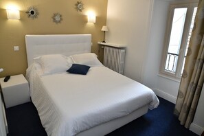 Une chambre d’hôtel avec un grand lit, une table de chevet, une lampe et une fenêtre avec des rideaux.
