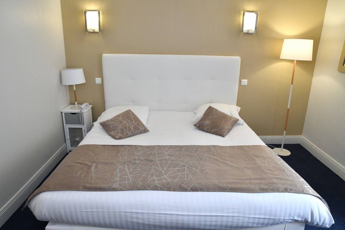 A hotel room with a large bed, two bedside lamps, and a nightstand with a phone.