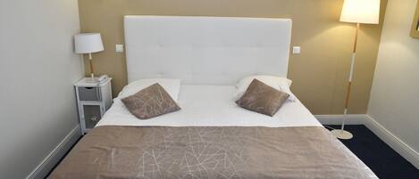 A hotel room with a large bed, two bedside lamps, and a nightstand with a phone.