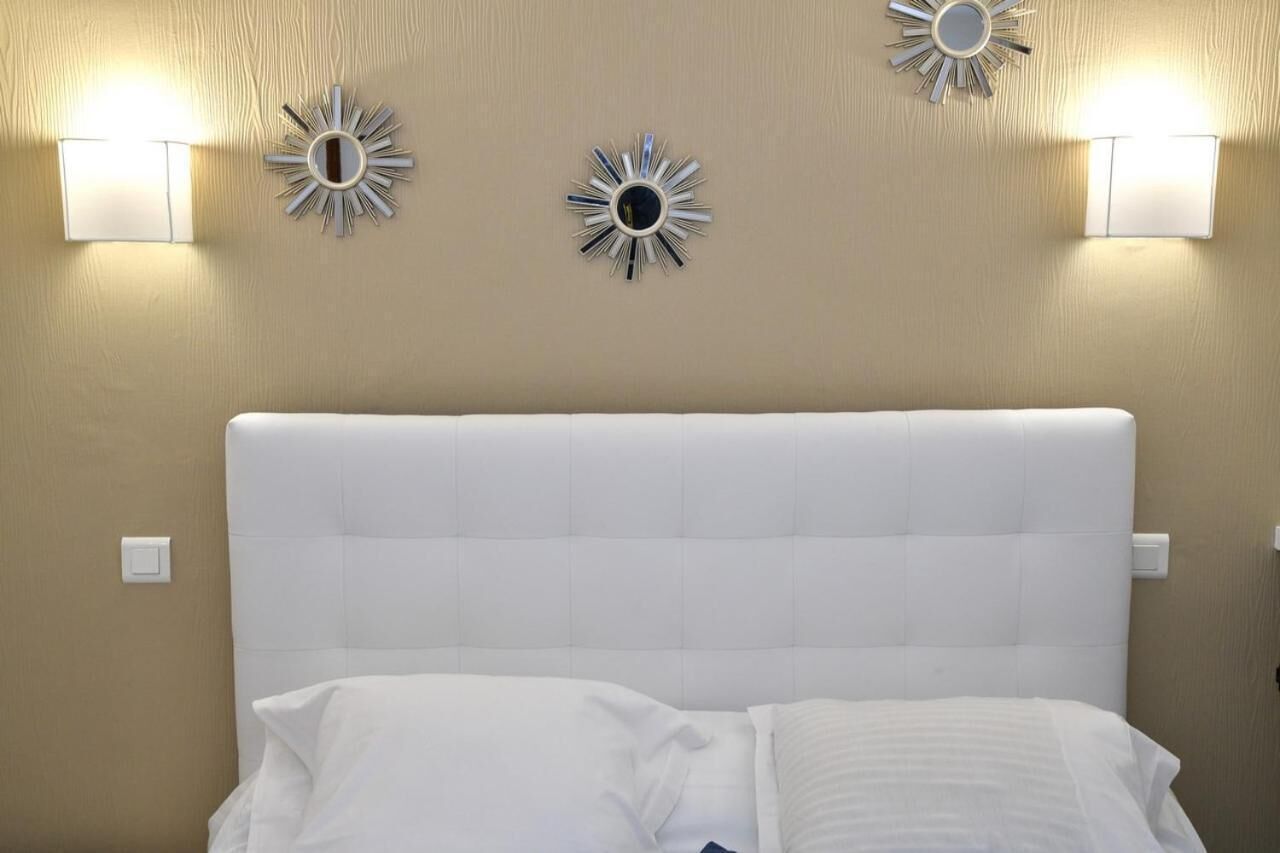 Una cama con cabecera blanca, dos lámparas fijadas a la pared y un espejo decorativo.