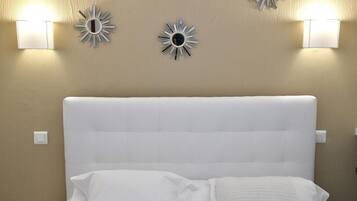 Una cama con cabecera blanca, dos lámparas fijadas a la pared y un espejo decorativo.