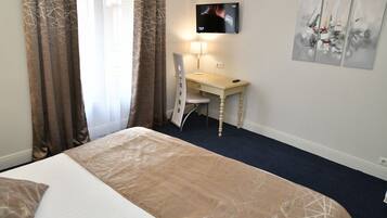 A hotel room with a bed, a desk, a chair, a TV mounted on the wall, and abstract artwork on the wall.