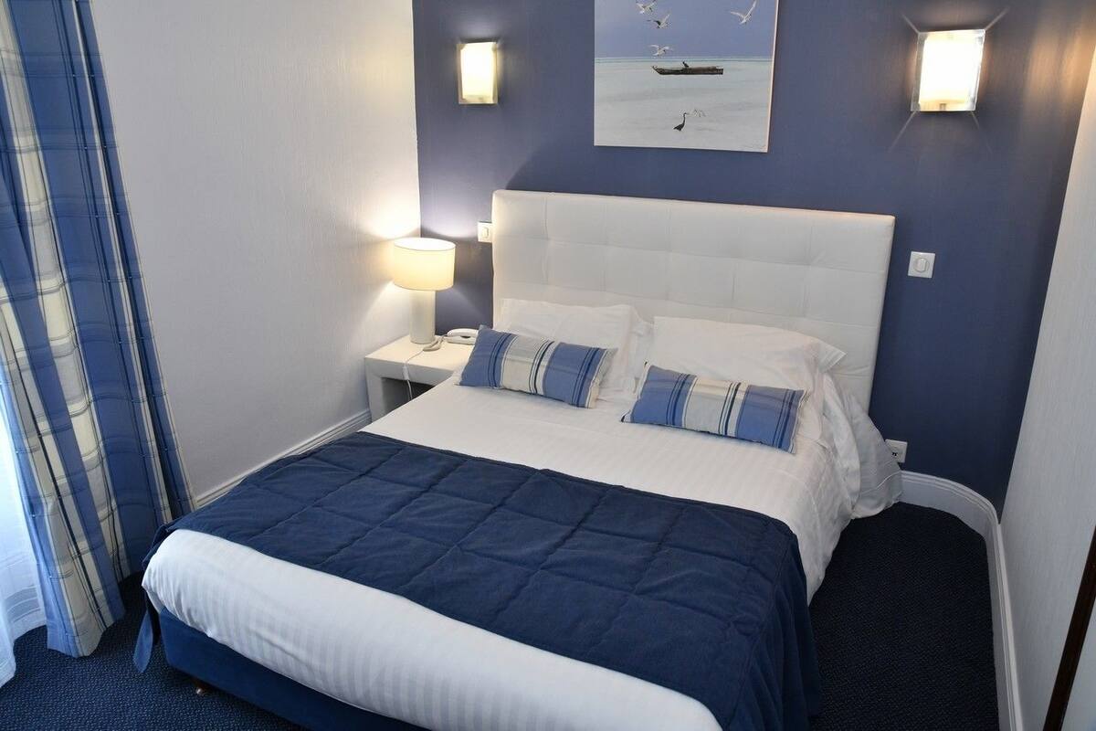A neatly made bed with a blue and white bedspread, a white headboard, and two bedside lamps.