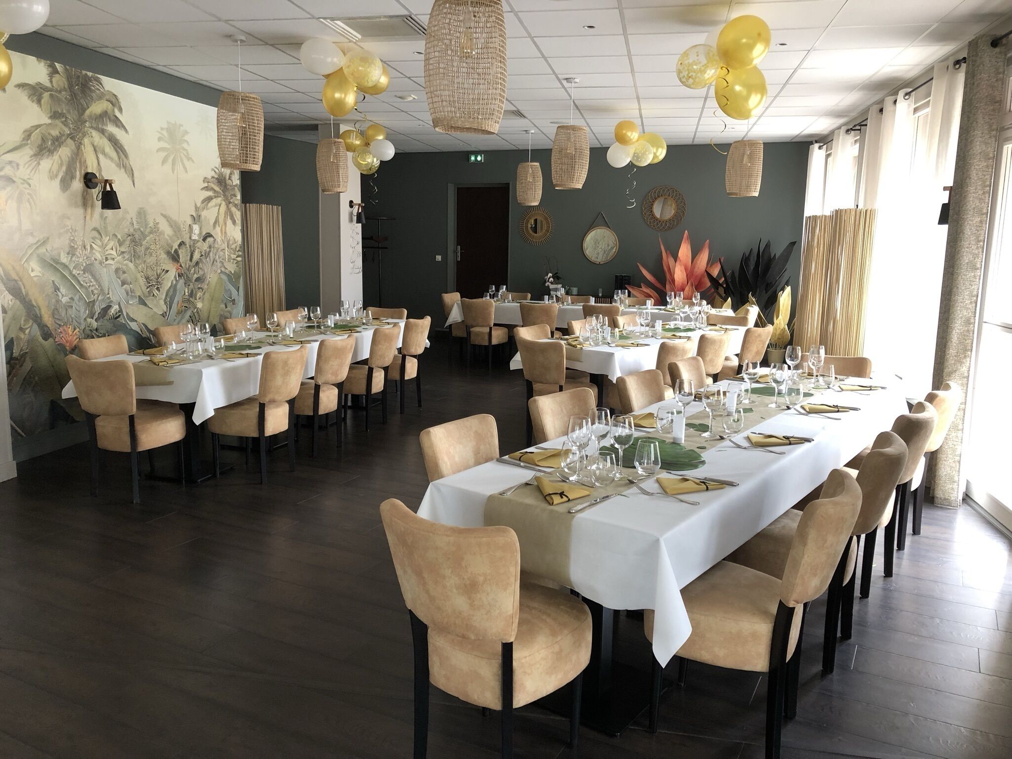 A spacious dining area with multiple tables set for a meal, featuring a tropical mural on the wall and decorative lighting.