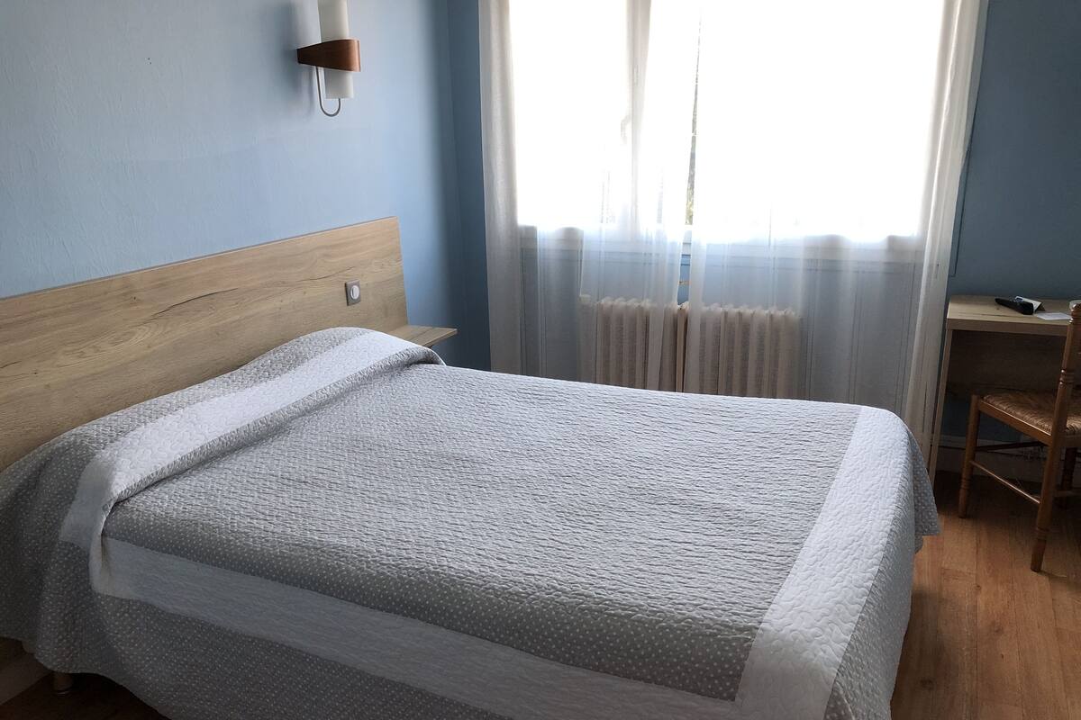 A neatly made bed with a wooden headboard, a bedside table with a remote control, and a chair.