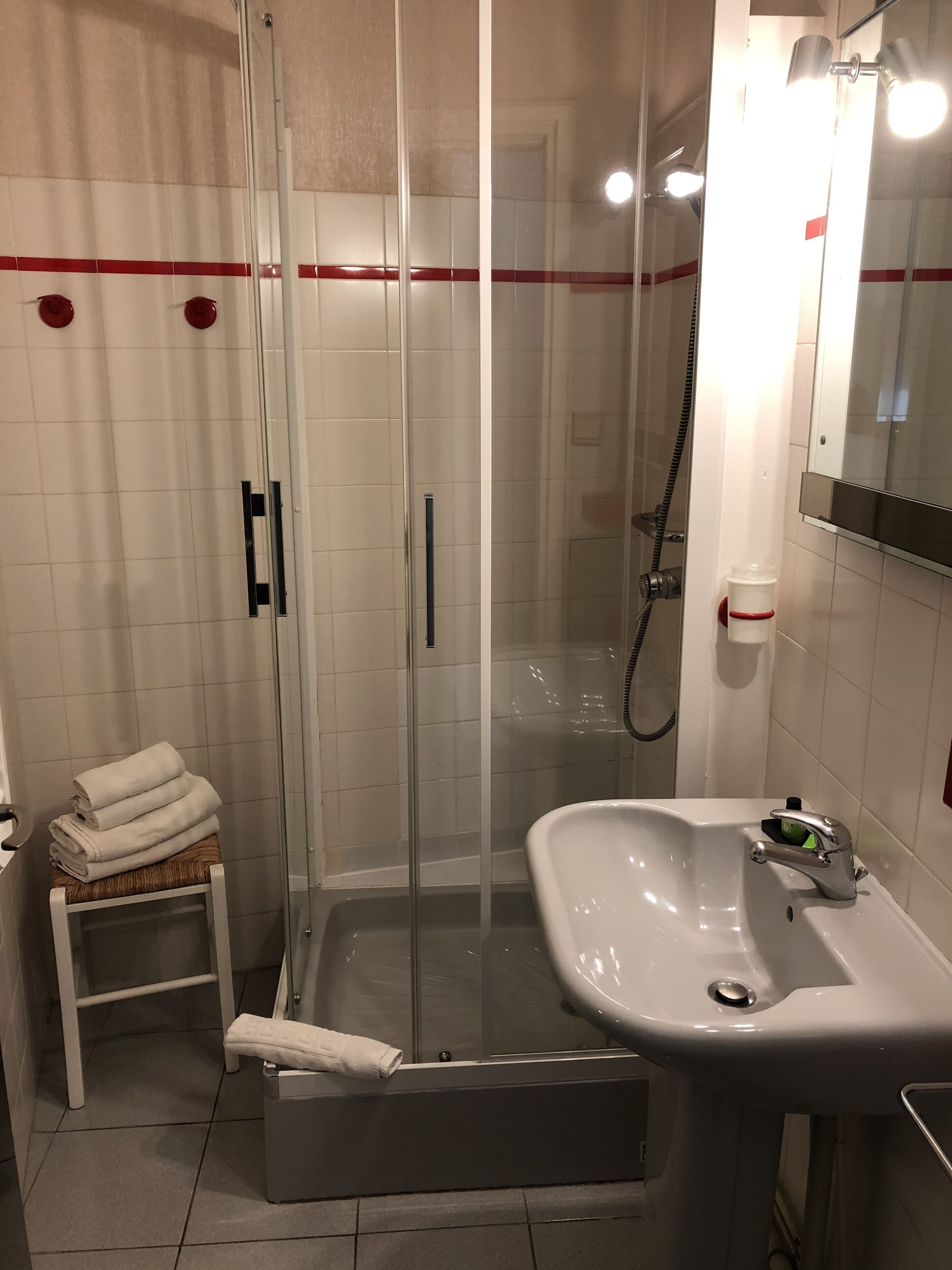 A bathroom with a glass-enclosed shower, a sink, and a small stool with towels.