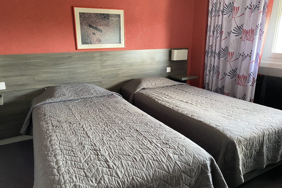A hotel room with two single beds, a wooden headboard, a framed artwork on the wall, and a patterned curtain.