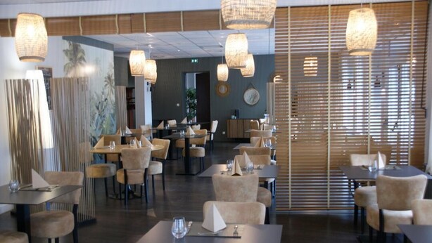 Un ristorante con diversi tavoli e sedie, lampadari in vimini appesi e un'ampia finestra con persiane.
