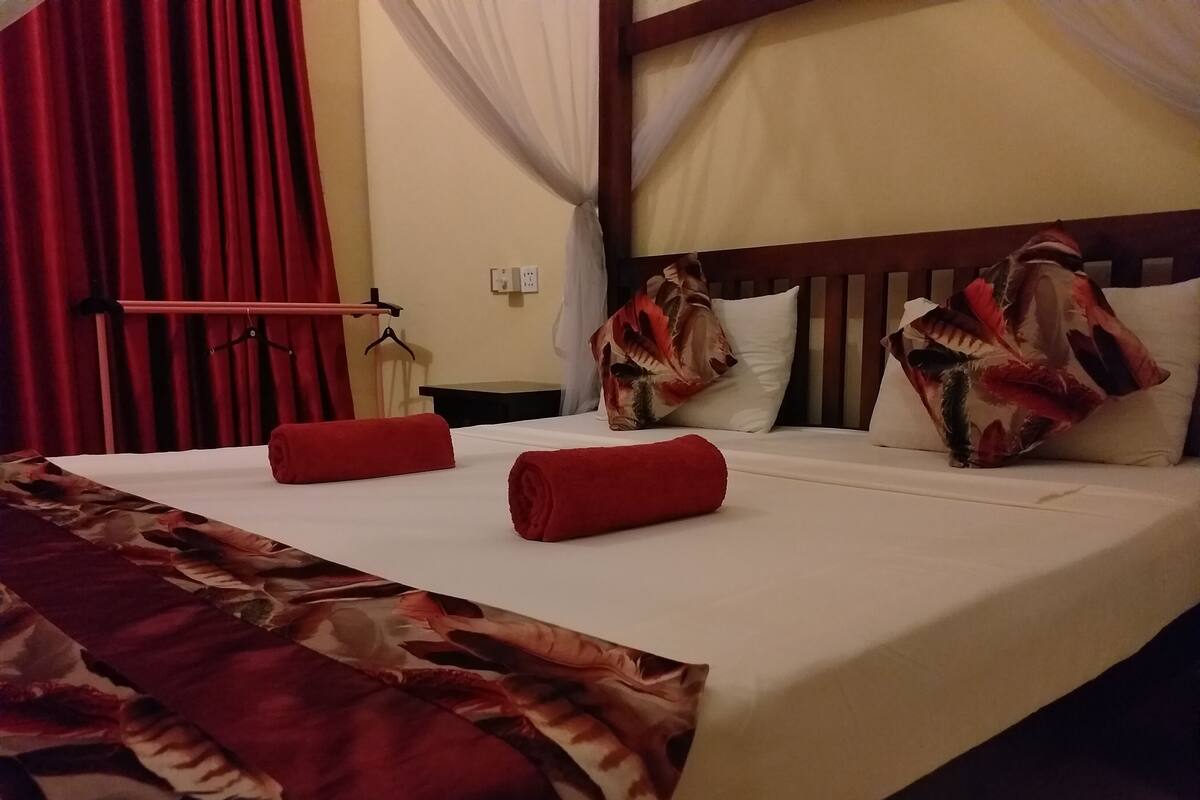 A hotel room with a bed, red towels, a floral bedspread, and a wooden headboard.
