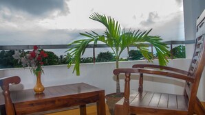 A wooden table and chair set on a balcony with a view of greenery and a cloudy sky.