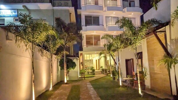 A multi-story hotel with a well-lit entrance, a paved pathway, and a small garden area with palm trees.