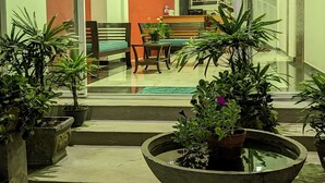 A modern interior with a staircase leading to a balcony, a dining area with a table and chairs, and several potted plants.