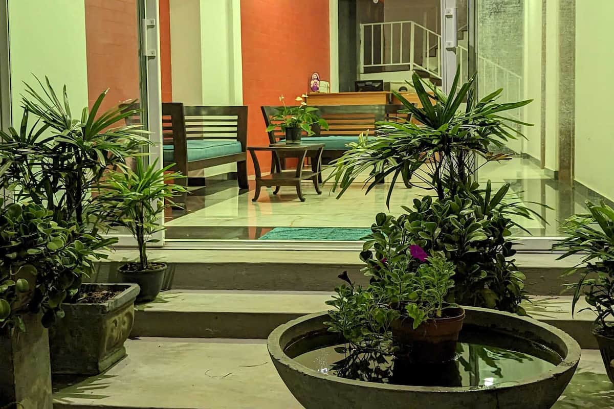 A modern interior with a staircase leading to a balcony, a dining area with a table and chairs, and several potted plants.