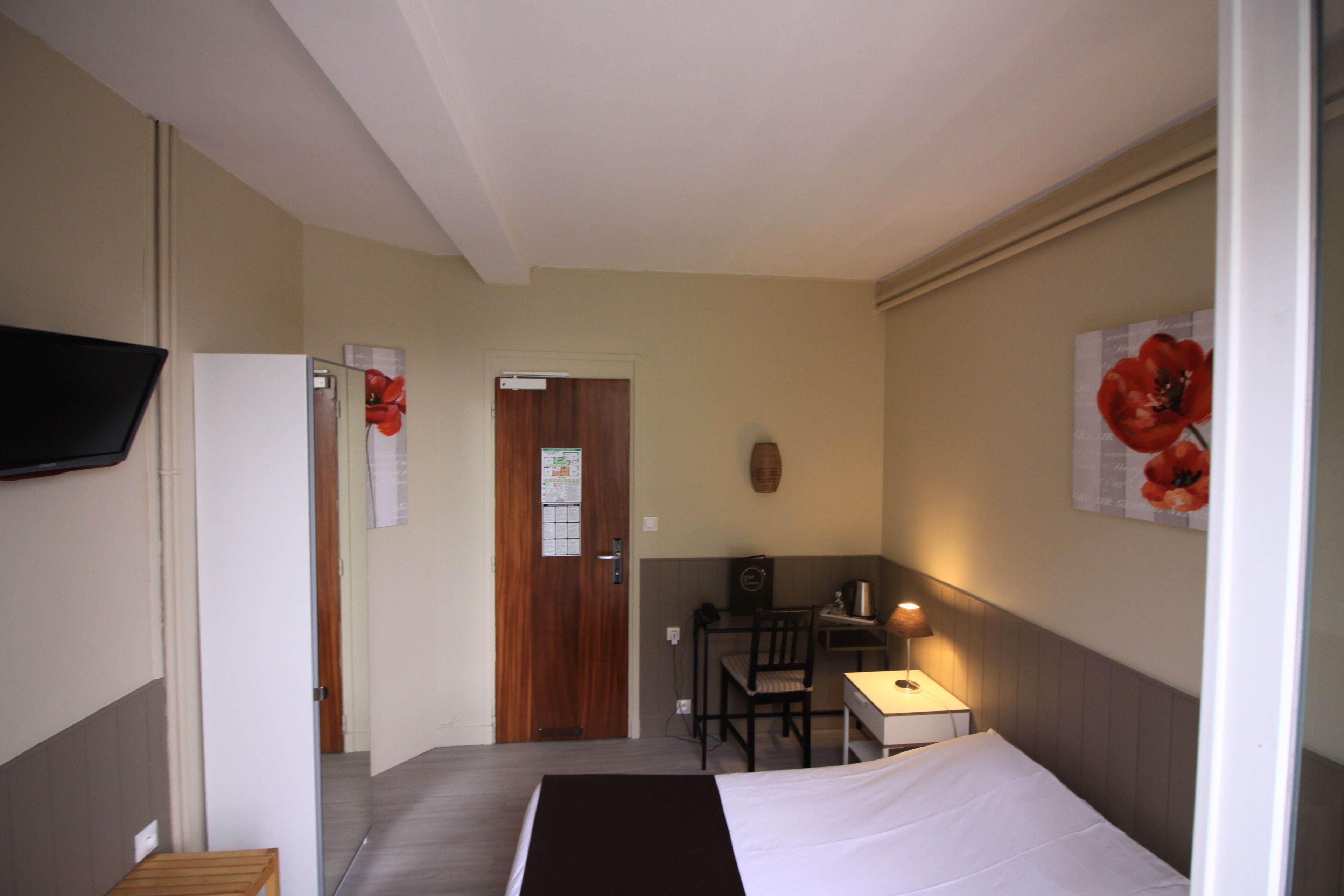 A hotel room with a bed, a desk, a chair, a television, and a door.