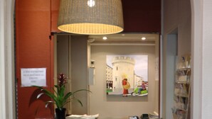 A reception area with a modern design, featuring a reception desk, a large hanging lamp, and a wall-mounted mirror. - Hôtel de L'Univers (Caen)