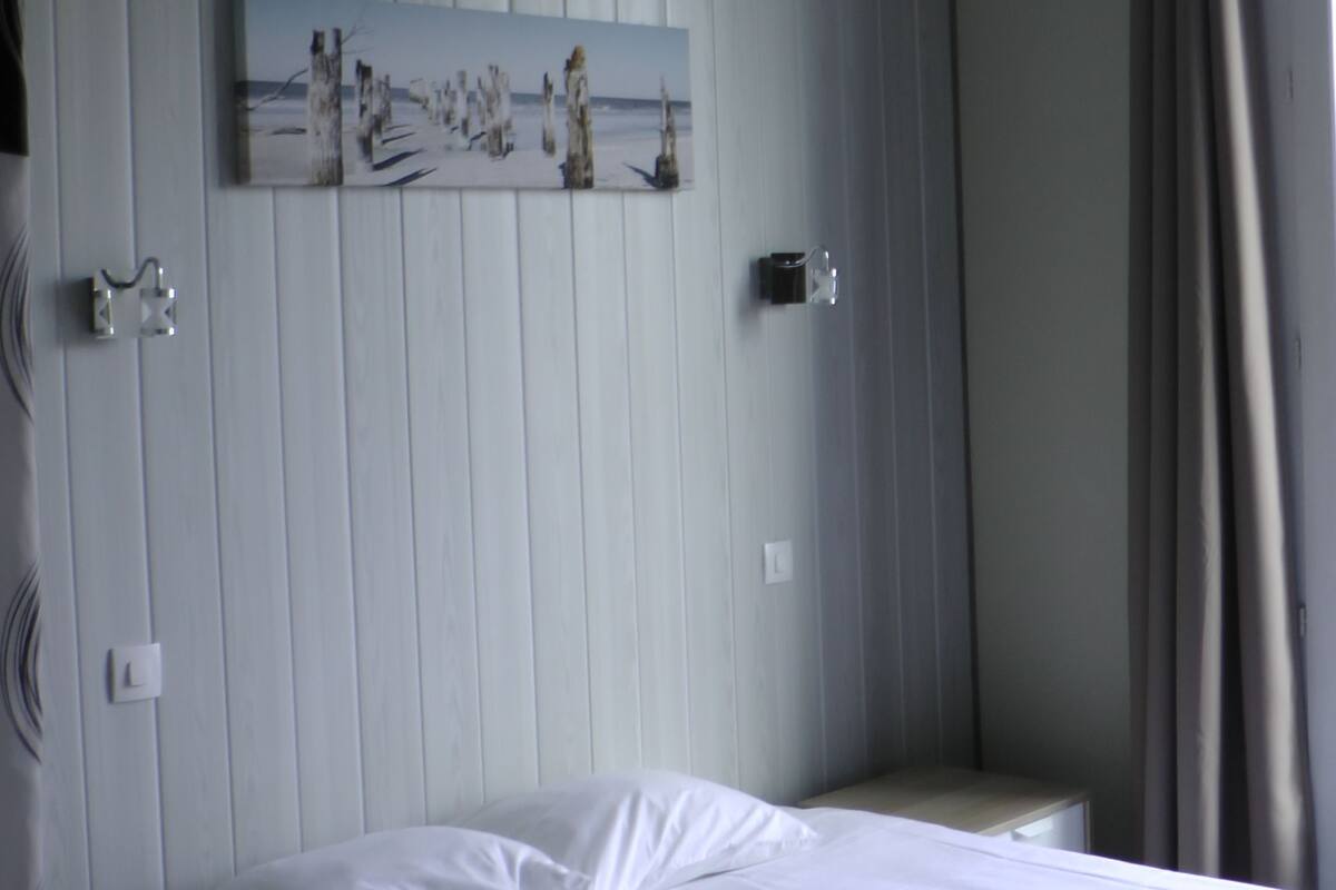A hotel room with a bed, a nightstand, a wall-mounted artwork, and a window with curtains.