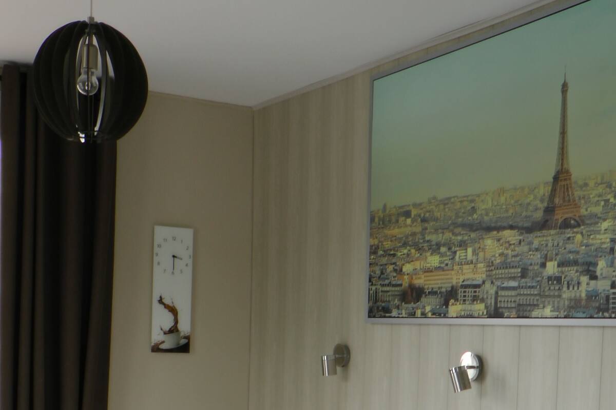 A hotel room with two beds, a radiator, a clock, and a painting of the Eiffel Tower.